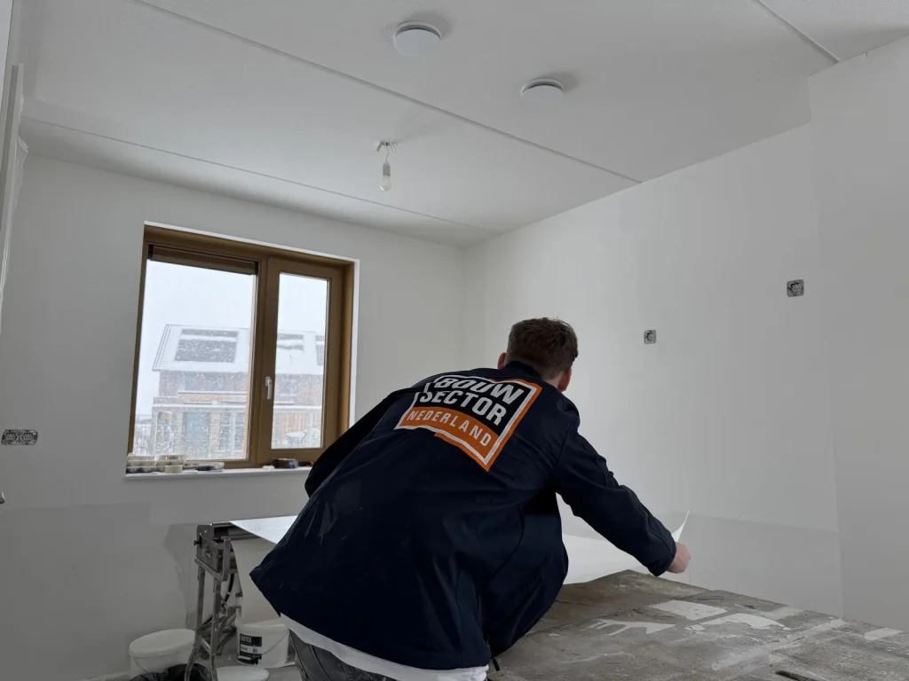 Behanger in donkerblauwe werkjas legt een baan vlies klaar op de plaktafel