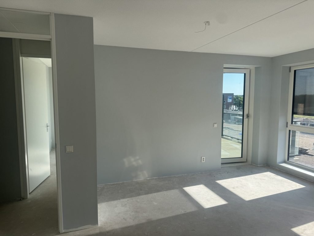 Appartement met lichtgrijs afgewerkte wanden en een deur naar het balkon