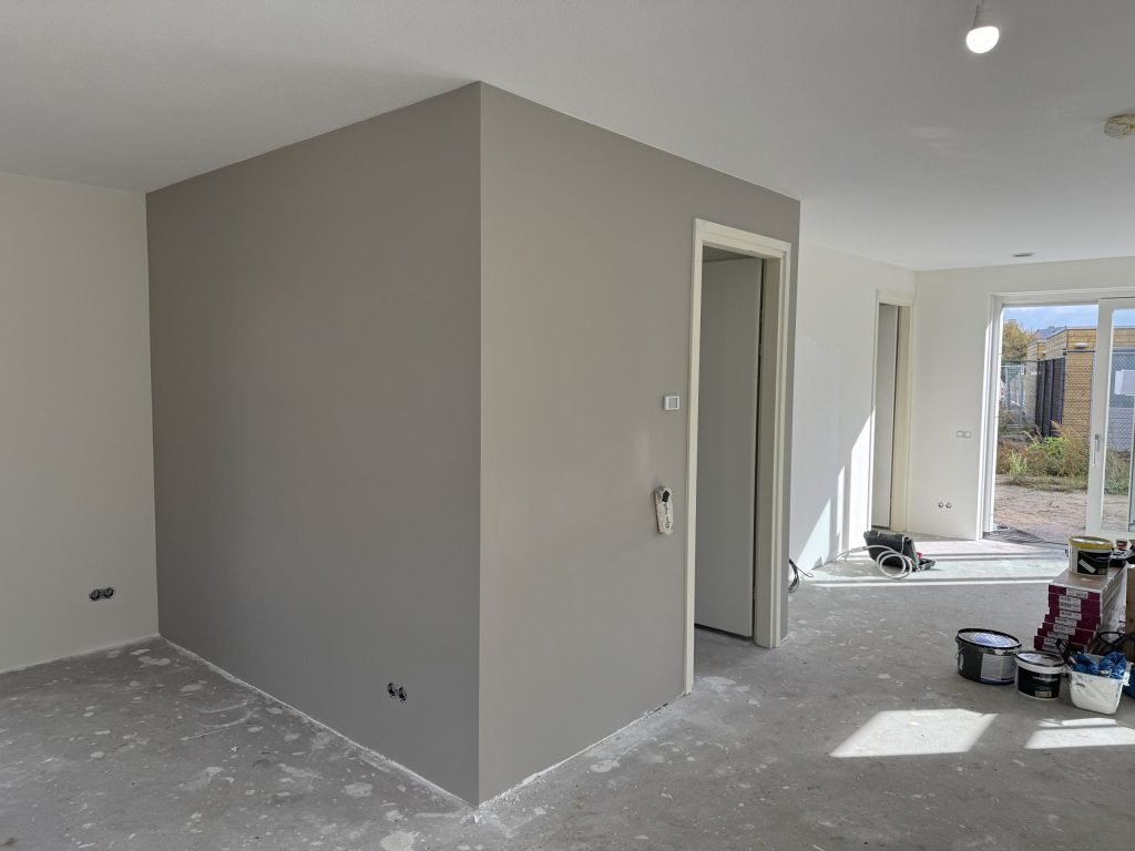 Pas gesausde wand in een warme grijstint met een deuropening en verfemmers op de vloer