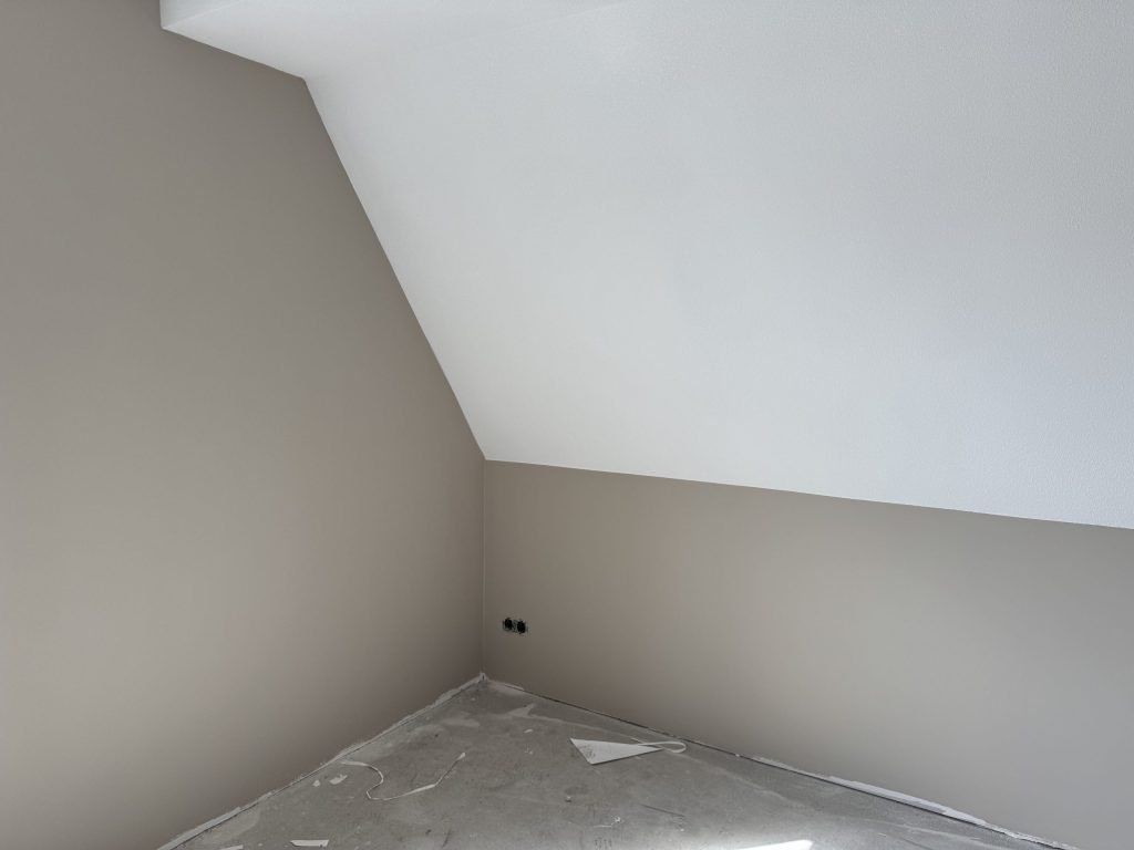 Slaapkamer onder het dak met een schuine wand, de muren glad afgewerkt in een lichte taupe kleur