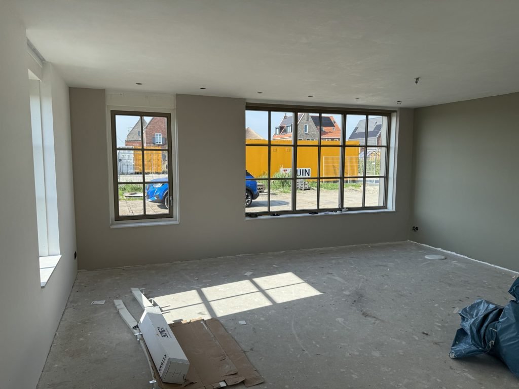 Woonkamer met warm grijze wanden, sprossenramen en zonlicht op de vloer van een nieuwe woning
